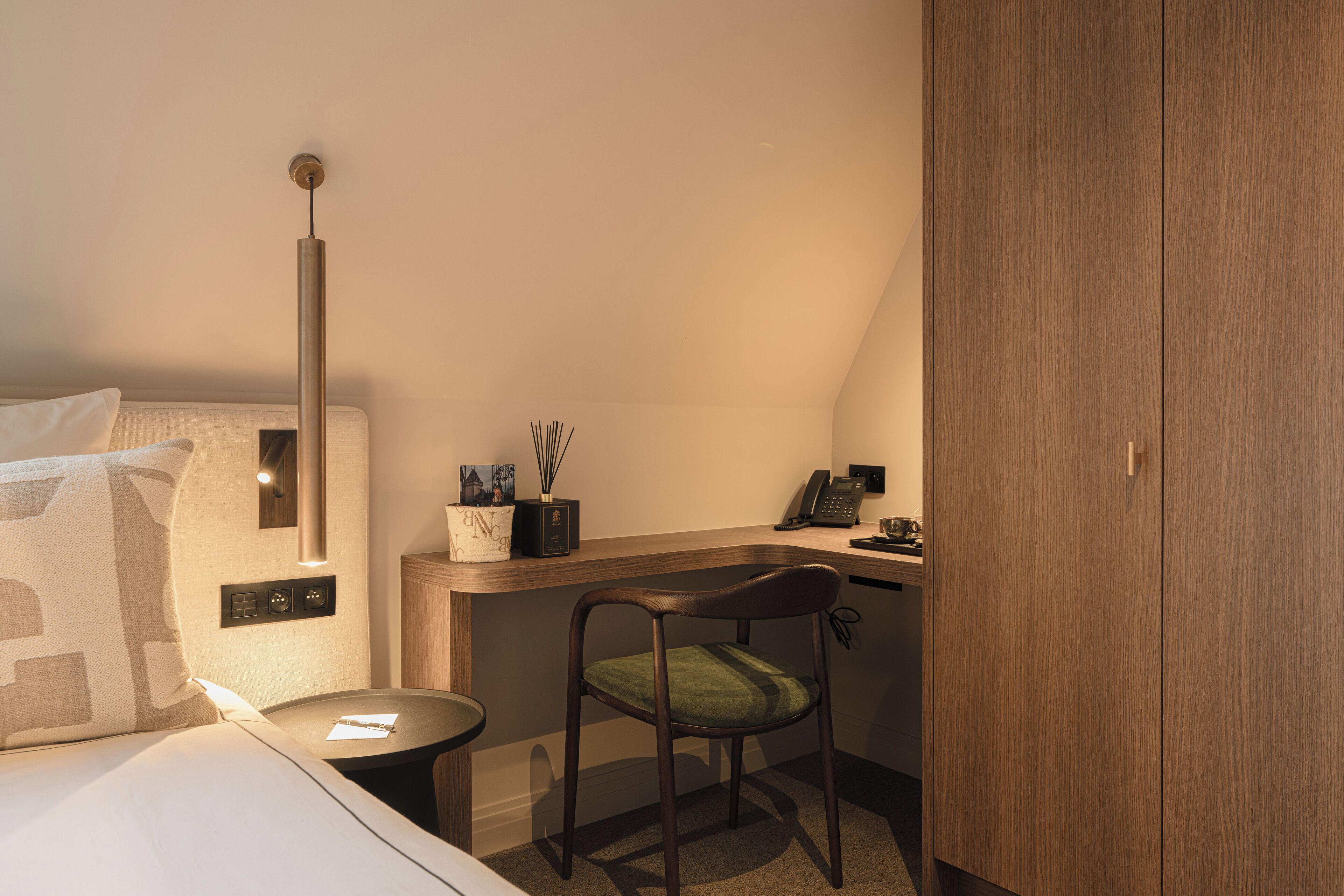 A hotel room with a bed, a desk, a chair, a lamp, and a wardrobe.