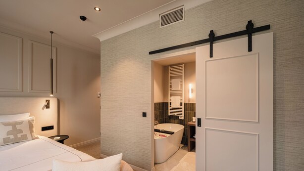 A modern hotel room with a large bed, a bathroom with a freestanding bathtub, and a sliding door. - Boutique Hotel Le Foulage (Bruges)