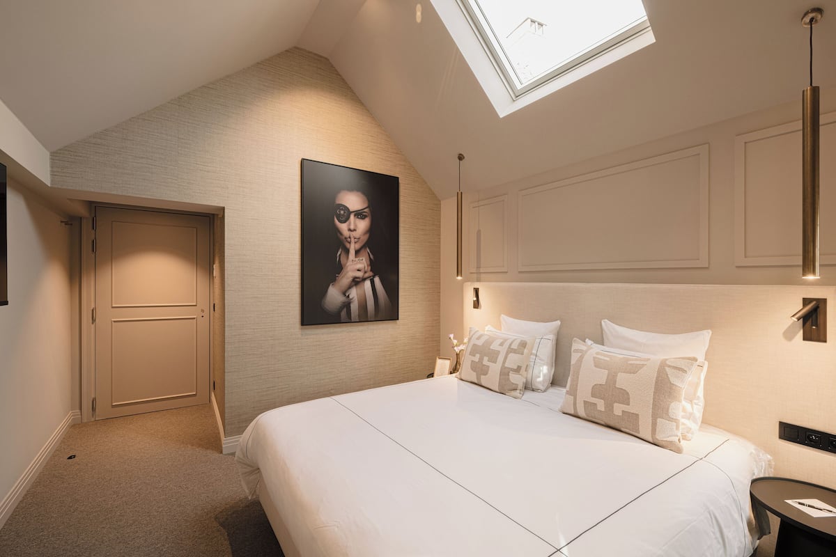 A bedroom with a skylight, a bed with white bedding, and a framed picture on the wall.