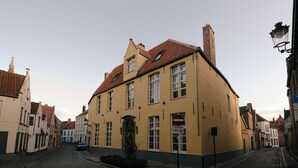 A narrow cobblestone street lined with historic buildings, including a yellow building with a black gate and a red-tiled roof. - Boutique Hotel Le Foulage (Bruges)