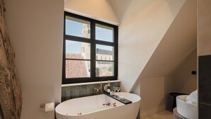 A modern bathroom with a freestanding bathtub, a window with a view of a building, and a wooden wall accent. - Boutique Hotel Le Foulage (Bruges)