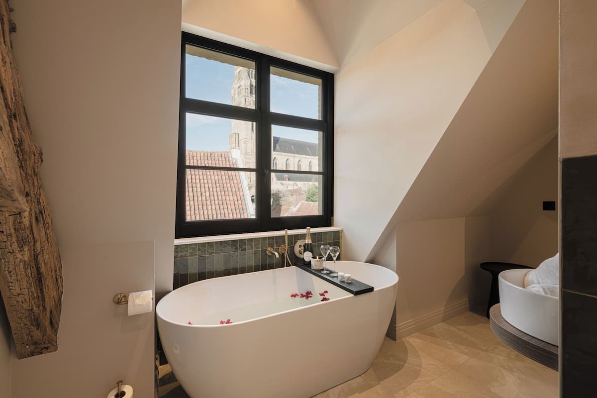 A modern bathroom with a freestanding bathtub, a window with a view of a building, and a wooden wall accent.