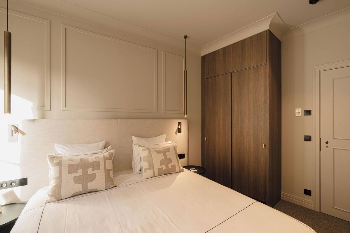 A hotel room with a large bed, two bedside tables, a wardrobe, and a pendant light.