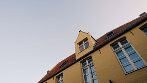 A building with a yellow facade, multiple windows, and a red-tiled roof. - Boutique Hotel Le Foulage (Bruges)