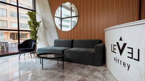 A modern lobby with a grey sofa, a round mirror, and a coffee table. A potted plant and a blue chair are visible. The wall has a wooden panel design. - New y modern apto In Virrey (Bogotá)
