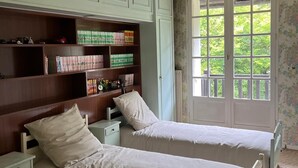 Ein Schlafzimmer mit zwei Einzelbetten, einem Holzregal und einem Fenster mit Blick auf Grünflächen.