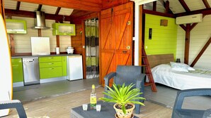 A compact room with a kitchenette, a bed, and a seating area with a potted plant.