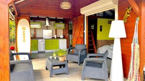 A cozy outdoor seating area with wicker furniture, a surfboard, and a kitchen visible through an open door.
