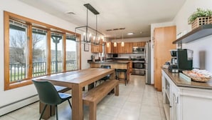 A modern kitchen with a wooden dining table, bar stools, and a large window.