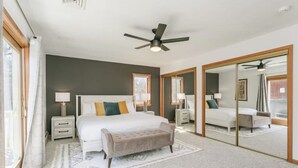 A bedroom with a large bed, bedside tables, a bench, a ceiling fan, and a sliding glass door leading to another room.