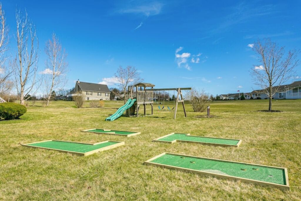 A grassy area with a swing set, a slide, and mini-golf holes.