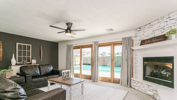 A living room with a fireplace, a ceiling fan, and a view of a swimming pool.