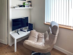A room with a white desk, a computer monitor, a gaming console, and a leather chair.