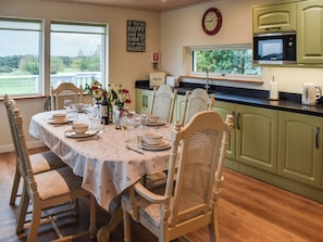 A dining area with a table set for four, chairs, a clock, and a microwave above the counter.