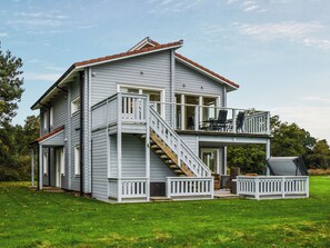 Una casa de dos pisos con balcón, escaleras y mobiliario exterior.
