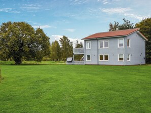Ett tvåvåningshus med ett rött tak, en balkong och en stor grön gräsmatta.