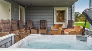 A deck with a hot tub, wicker chairs, and a door.