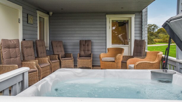 Una terraza con un jacuzzi, sillas de mimbre y una puerta.