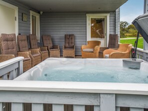 Una terraza con un jacuzzi, sillas de mimbre y una puerta.
