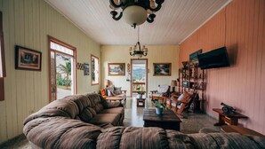 A cozy living room with a large sectional sofa, a wooden coffee table, and a television mounted on the wall. There are several framed pictures on the walls and a window with a view of the outdoors. - Antique Mountain Cabin (Ponce)