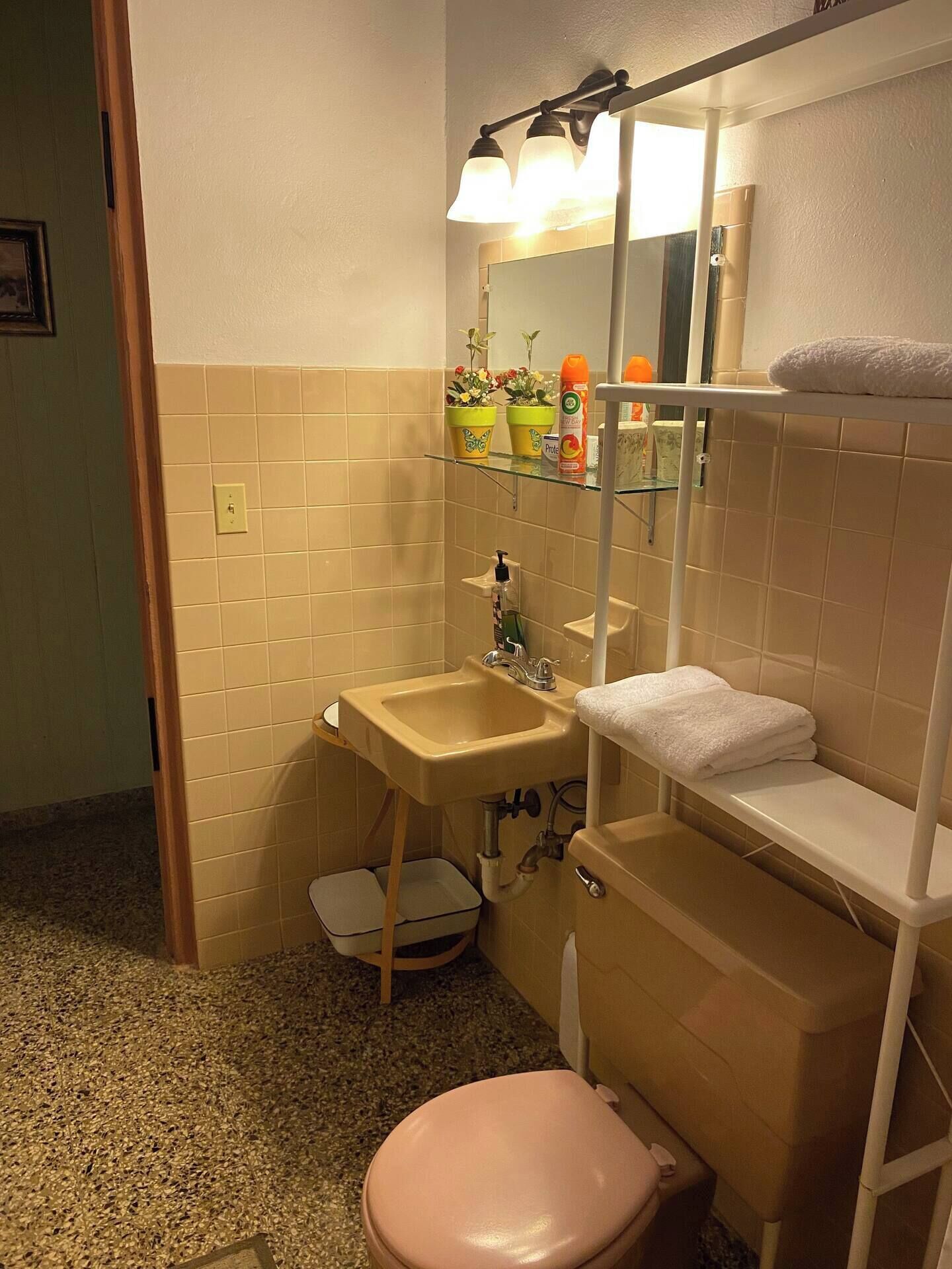Un baño con lavamanos, inodoro y repisas con artículos de tocador.