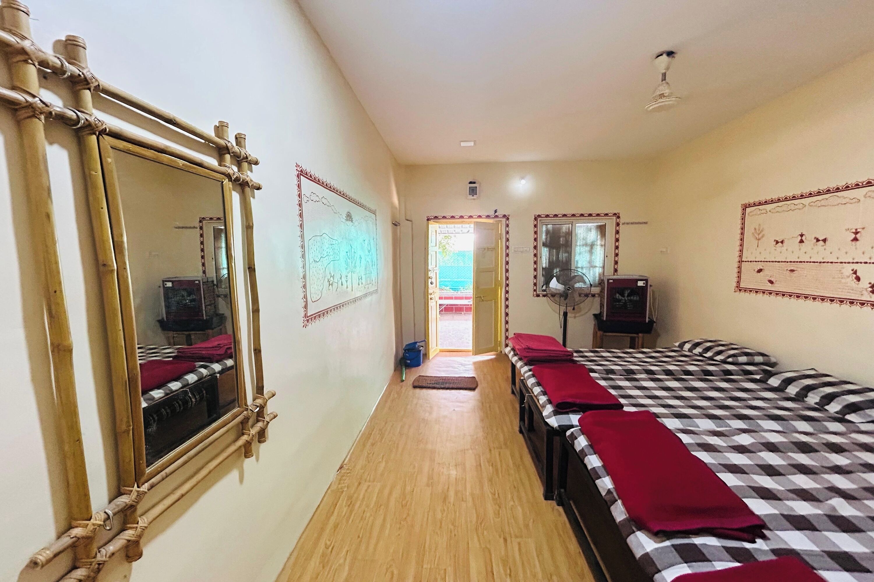 A hotel room with a bamboo-framed mirror, a checkered bedspread, and a view of the sea through an open door.