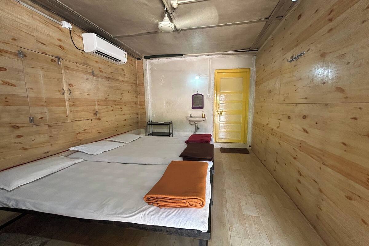 A room with wooden walls, a bed with white and orange linens, a sink, and a yellow door.