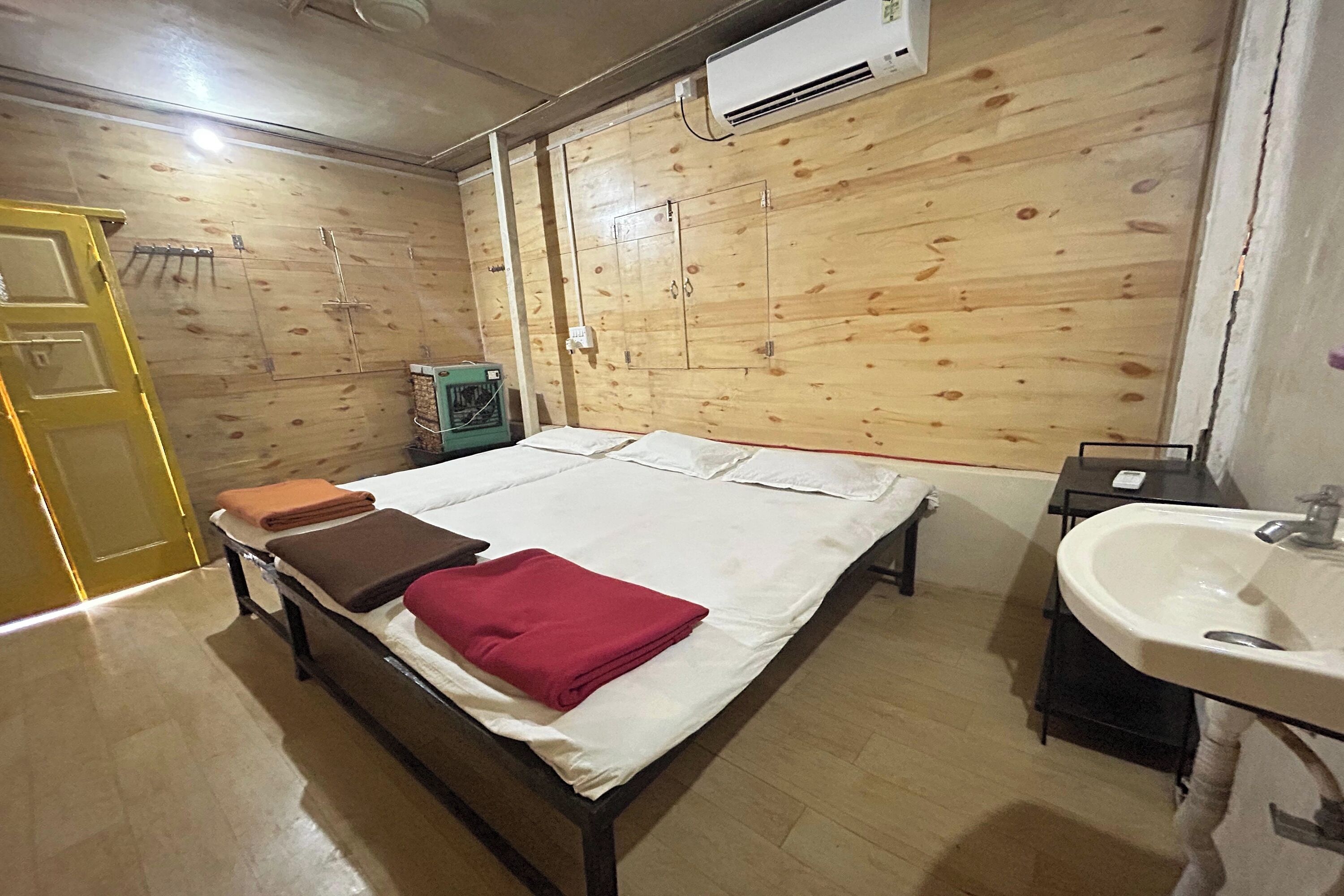 A room with a bed, a bedside table, a sink, and a wooden wall with a door.
