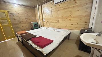 A room with a bed, a bedside table, a sink, and a wooden wall with a door.
