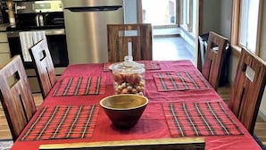 A dining area with a red tablecloth, wooden chairs, a bowl, and a kitchen in the background.