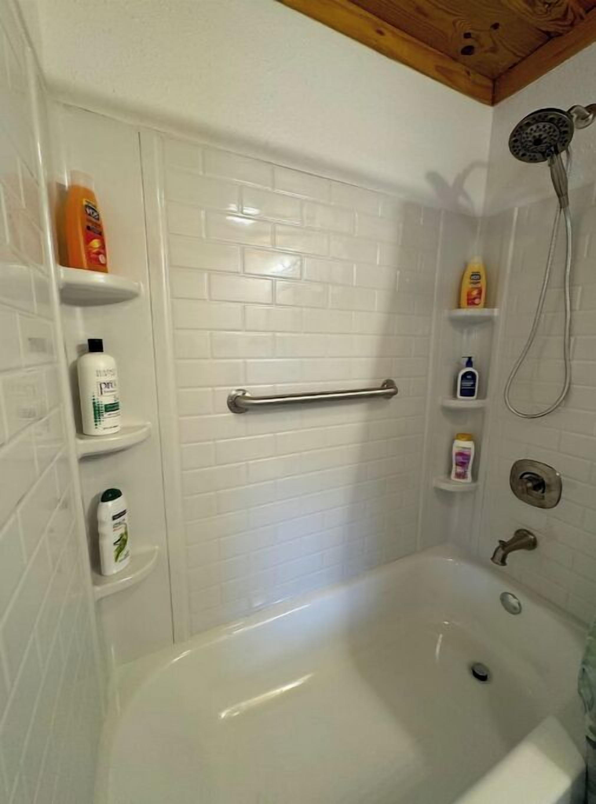 A bathroom with a bathtub, a shower, and a handrail. There are shelves with toiletries.
