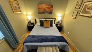 A hotel room with a bed, nightstands, a bench, and artwork on the walls.