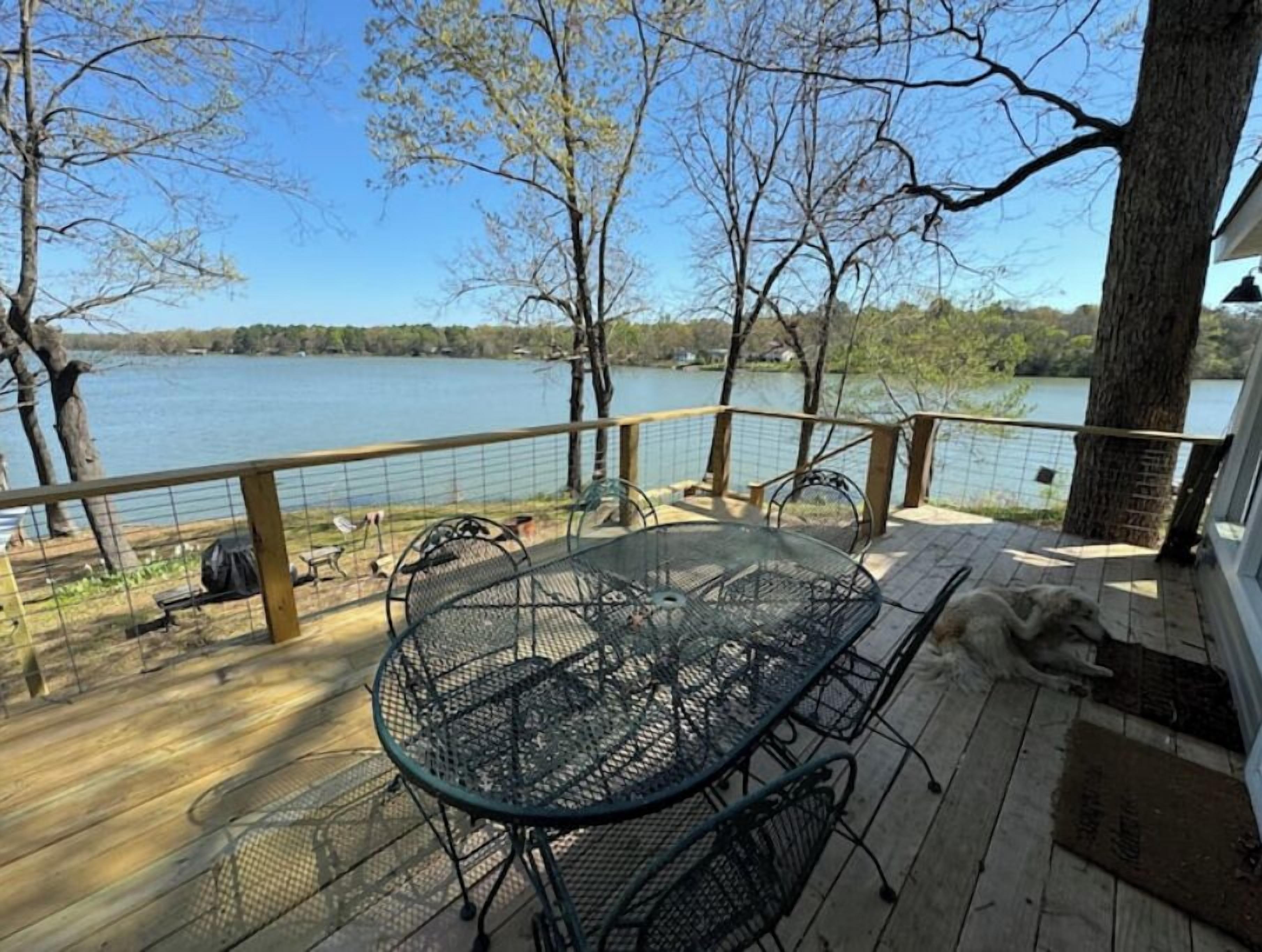 Eine Terrasse mit Glastisch und Stühlen mit Blick auf einen See.