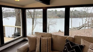 A room with a large window overlooking a lake, a cushioned seating area, and a ceiling with exposed beams.
