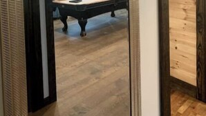A room with a pool table, a ceiling fan, and a large mirror reflecting the room.