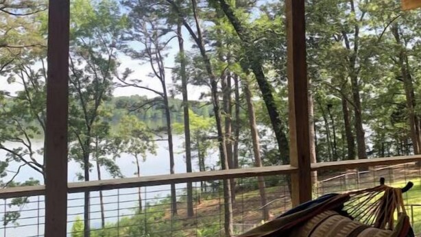 A hammock under a wooden ceiling with a view of a lake and trees.