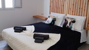 A modern bedroom with a bed, wooden slat headboard, and a hanging light fixture. - Azure Sunset (Mosteiros)