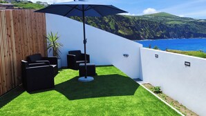 A patio with a black umbrella, black outdoor furniture, and a view of the ocean and hills. - Azure Sunset (Mosteiros)