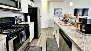 Een moderne keuken met witte kasten, een zwarte kookplaat, roestvrijstalen apparatuur en granieten aanrecht.