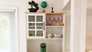 Ett köksutrymme med ett skåp som innehåller glas, en grön vattenkokare och muggar.