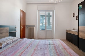 A bedroom with a bed, a wardrobe, a radiator, and a window with a view of buildings.