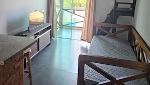 Ein gemütliches Zimmer mit Bett, Schreibtisch und Fernseher. Ein Glastür führt zu einem Balkon mit Blick ins Grüne.