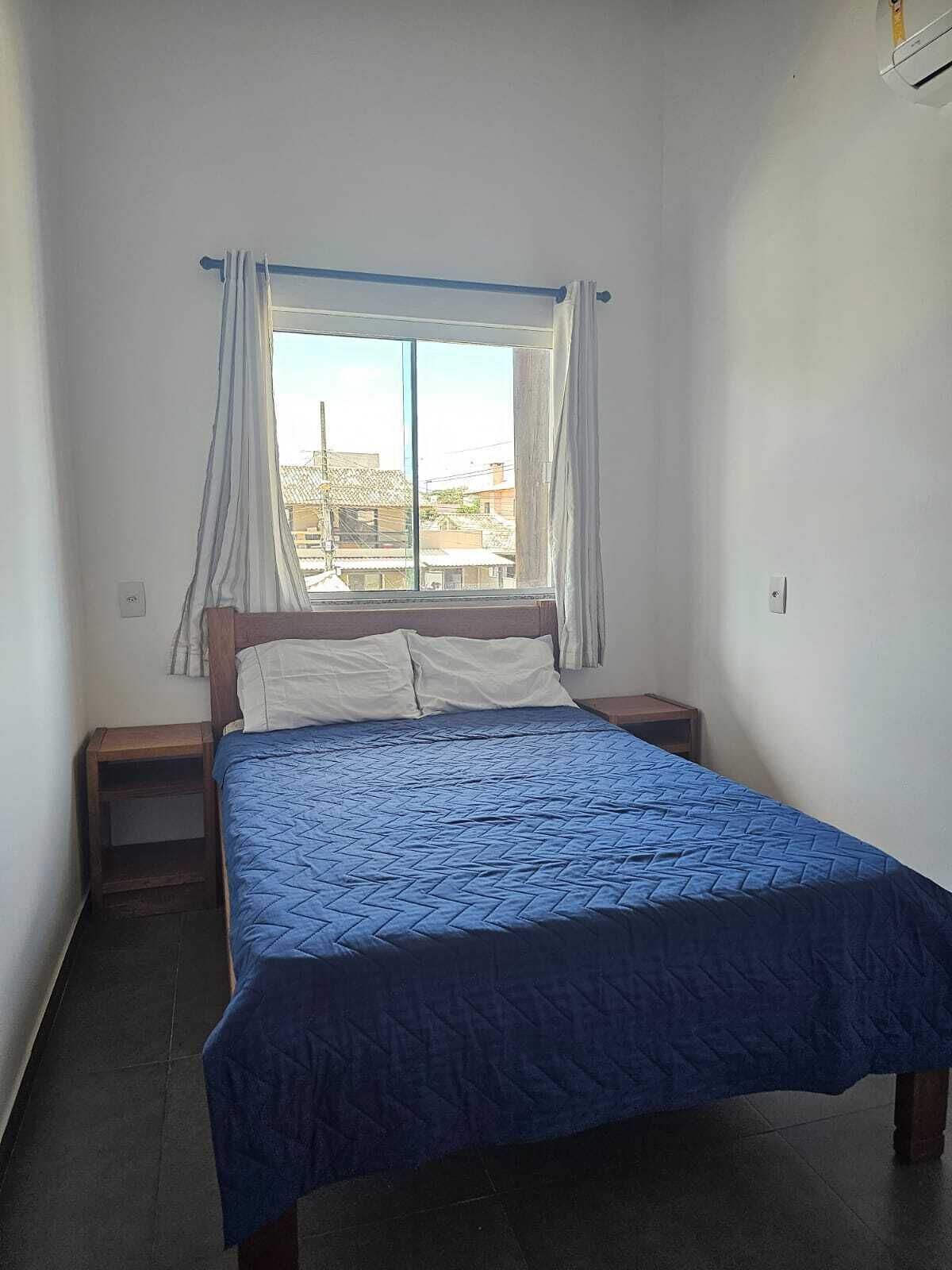 Een slaapkamer met een bed, een raam met gordijnen, een nachtkastje en een stopcontact.