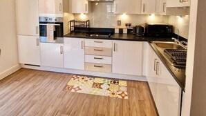 A modern kitchen with white cabinets, a stainless steel range hood, and a wooden floor. - The Mirrored House (Whole Flat) (Darford)