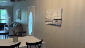 Un coin repas avec une table, des chaises et un lustre. Il y a un tableau au mur et une fenêtre avec des rideaux.
