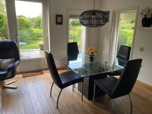 A modern dining area with a glass table, black chairs, and a hanging light fixture.