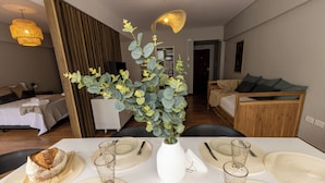 A dining area with a white table set for four, a white vase with green foliage, and a loaf of bread on the table.