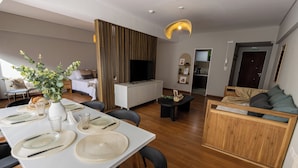 A modern living room with a dining area, wooden flooring, and a flat-screen TV.