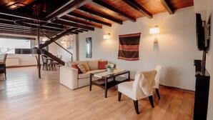 Ein modernes Wohnzimmer mit Treppe, Holzböden, einer Couch, einem Couchtisch und einem an der Wand befestigten Fernseher.