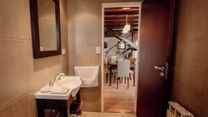 Ein Badezimmer mit Waschbecken, Spiegel und Handtuchhalter. Eine Tür führt zu einem Essbereich mit Tisch und Stühlen.